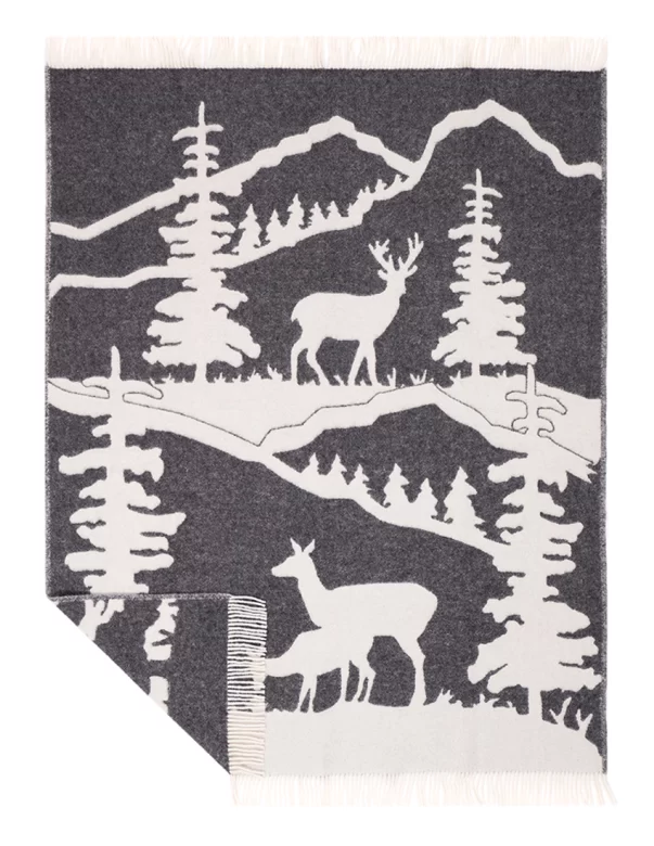 A wool blanket depicting a scenic mountain landscape with white deer and trees against a gray background, including fringe edges, made by weaving mill Barker Textiles.