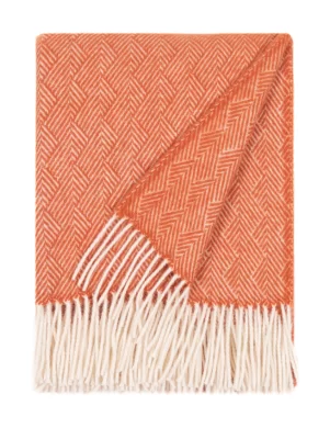 A wool blanket with a herringbone pattern in orange and white, finished with white fringes, made by weaving mill Barker Textiles.