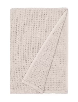 Beige blanket featuring a waffle weave texture, neatly folded with one corner flipped to reveal the underside, made by weaving mill Barker Textiles.