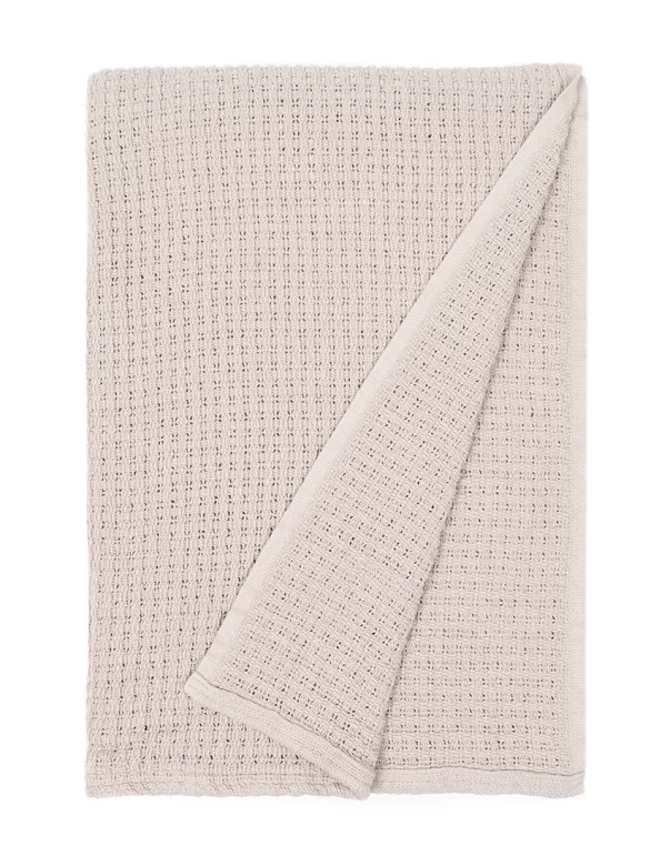 Beige blanket featuring a waffle weave texture, neatly folded with one corner flipped to reveal the underside, made by weaving mill Barker Textiles.