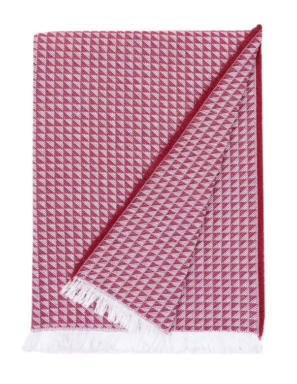 A cotton throw with a red and white checkered pattern, folded to show the reverse side. The edges are adorned with white fringes, made by weaving mill Barker Textiles.