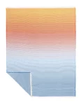 A cotton blanket with a gradient design transitioning from orange to light blue, creating a modern ombre effect, made by weaving mill Barker Textiles.