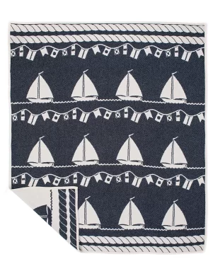 Navy blue blanket adorned with white sailing boats and nautical flags, neatly folded with one corner flipped to reveal the reverse side, made by weaving mill Barker Textiles.