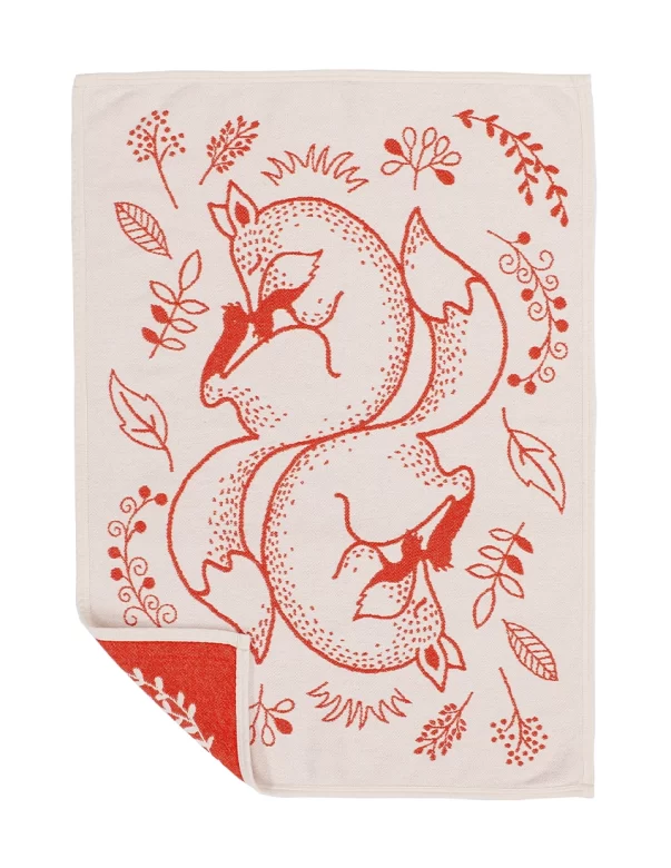 A baby blanket with a design of two intertwined red foxes surrounded by foliage on a cream background, with a folded corner revealing the reverse side made by weaving mill Barker Textiles.